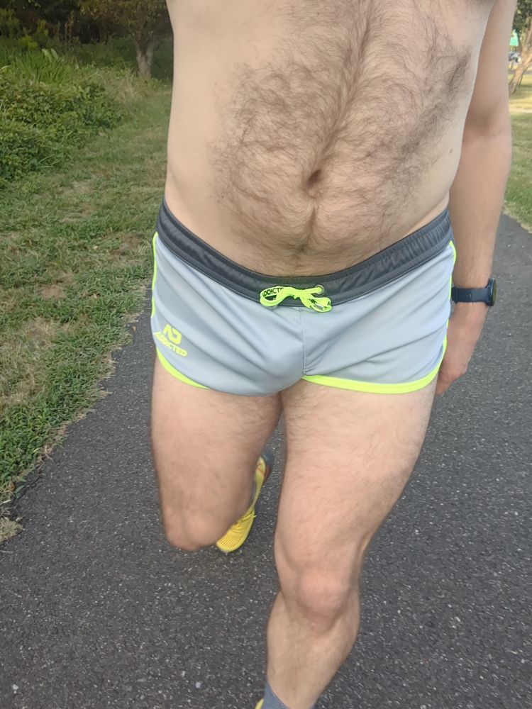 A dude wearing a pair of grey running shorts with neon yellow trim and yellow running shoes walking on a bike trail 