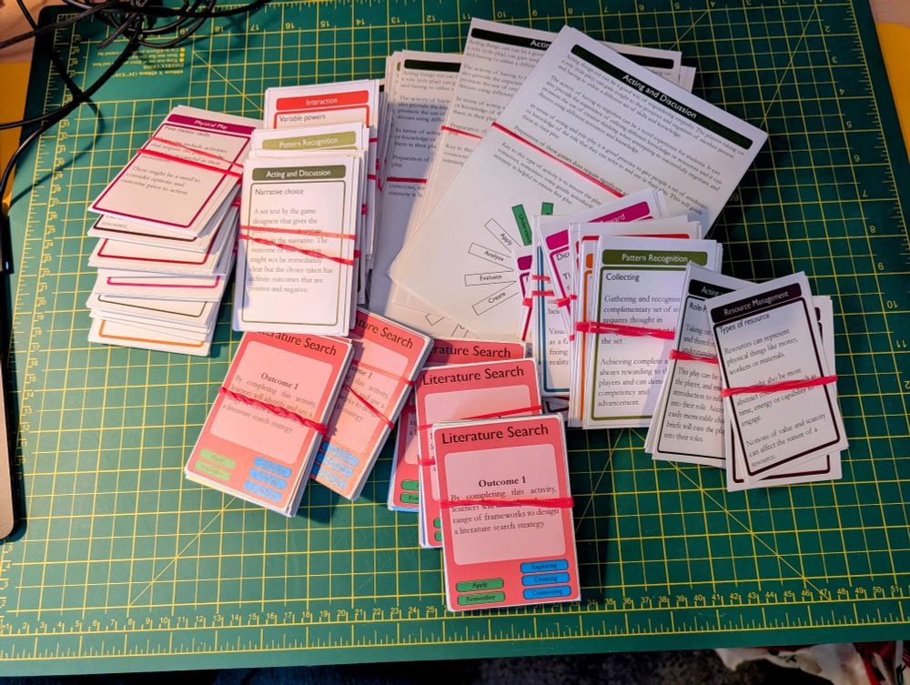 Piles of cards on a cutting mat. They have game mechanics and learning objectives on them for use in a playful learning workshop 