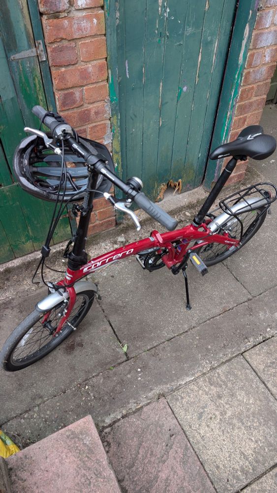Red folding bike in back yard UK.