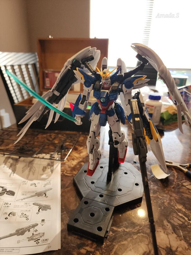 A white and blue mecha with red accents holding a beam saber in the right hand and a beam rifle in the left. It has white angelic wings. 