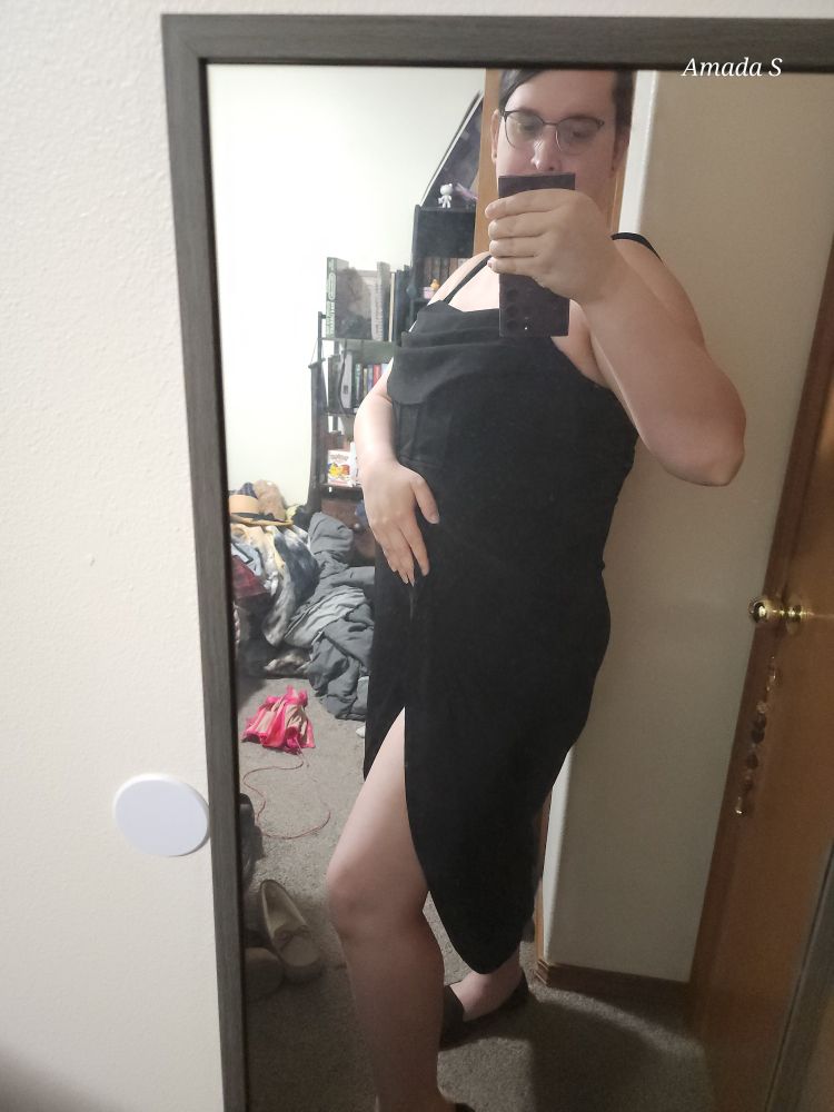 Amada wearing a black dress. It has a ribbed top and straps with a rumbled fabric over the bust.

She has pulled the split skirt and stick a leg out on display.