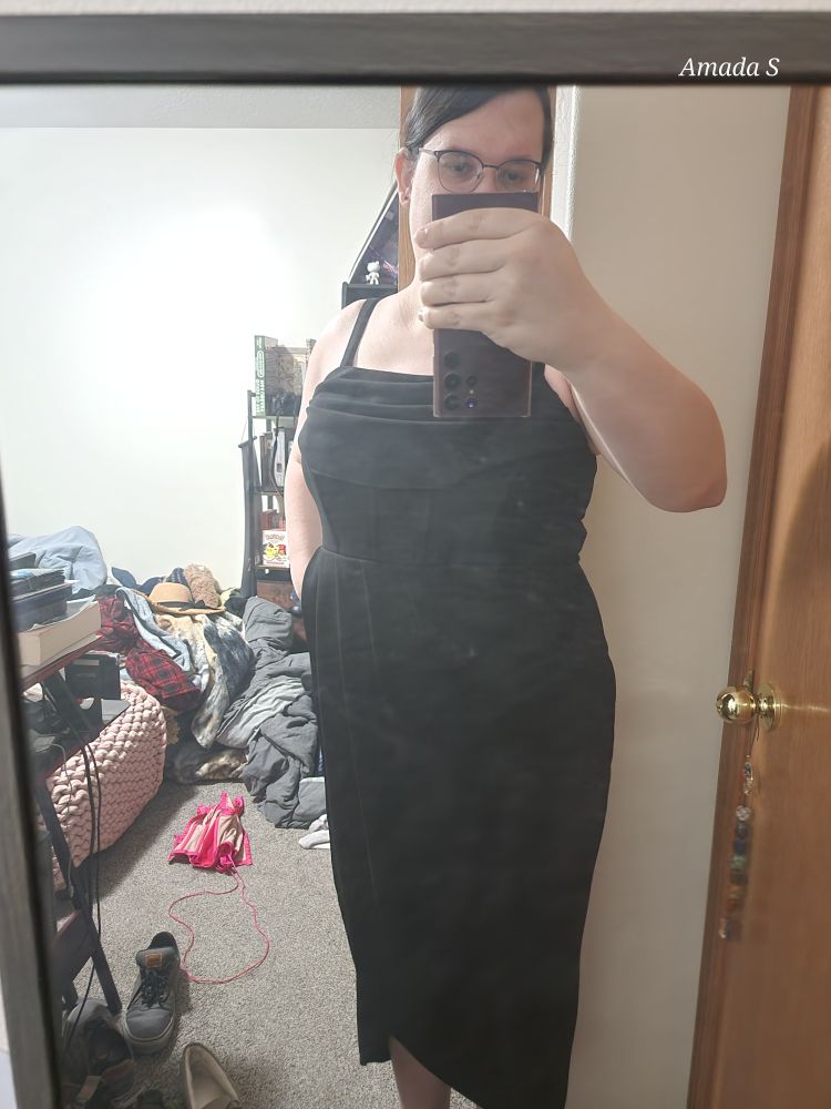 Amada wearing a black dress. It has a ribbed top and straps with a rumbled fabric over the bust. 