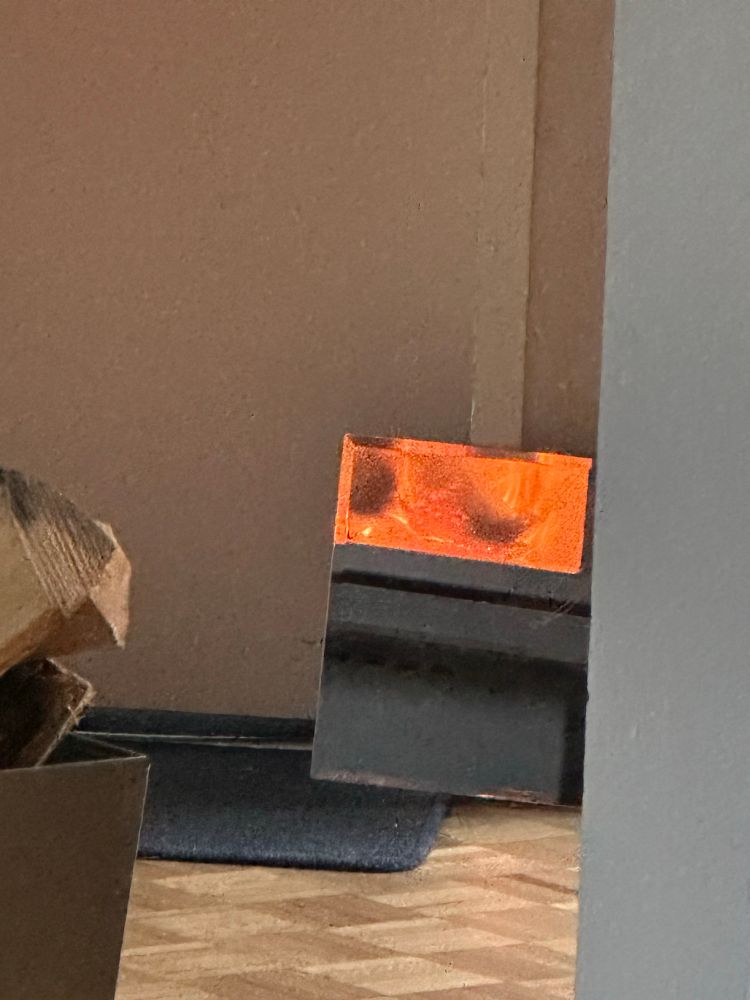 The mirror reflection of the flames from my wood burner in the hallway. Woodbox is in the foreground. The mirror is placed against a wall so I can see the flames from my bed. 