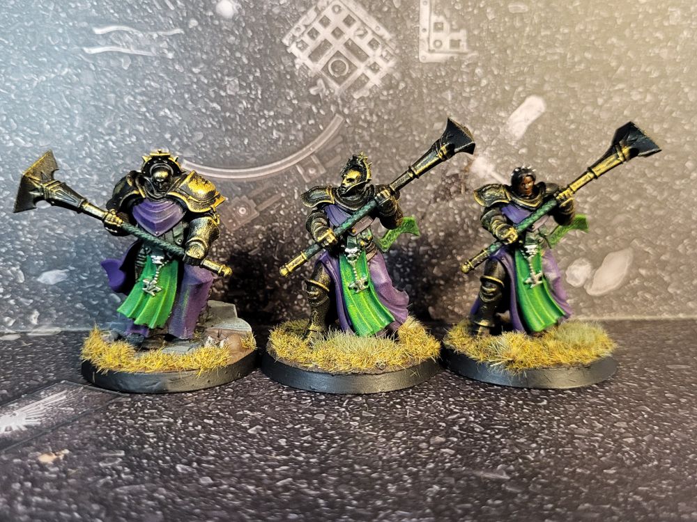 Three Stormcast Eternals models, armour black with a gold patina, wearing green and purple robes.