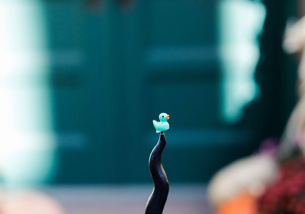 A tiny aqua color duck with a magnet on the bottom connected to a railing in the Chelsea neighborhood by a tiny magnet.