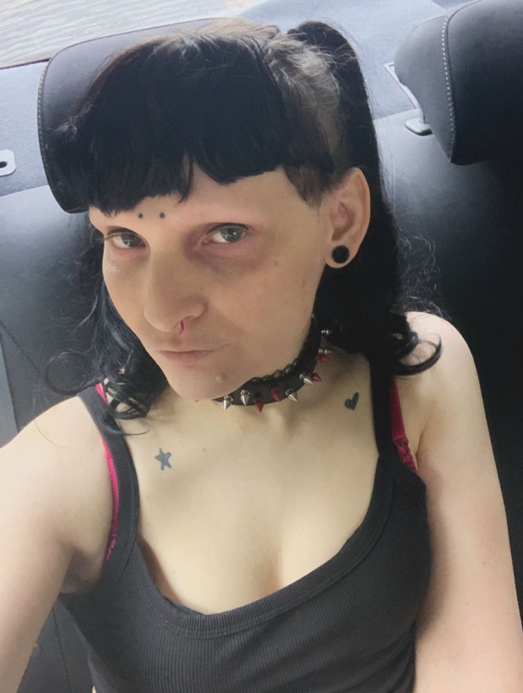 a selfie of zero, it has a black tank top, and black/red spiked collar on. it has black hair and bangs with pigtails 