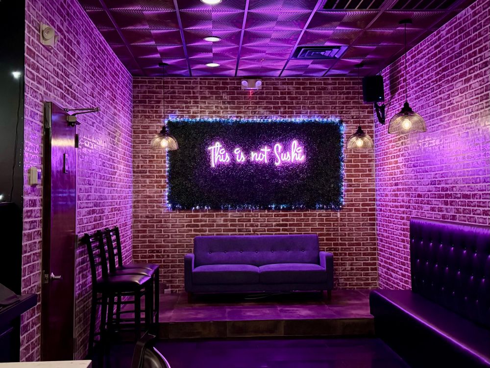 A bricked room washed in violet light from a neon sign reading “This is not Sushi” in script.