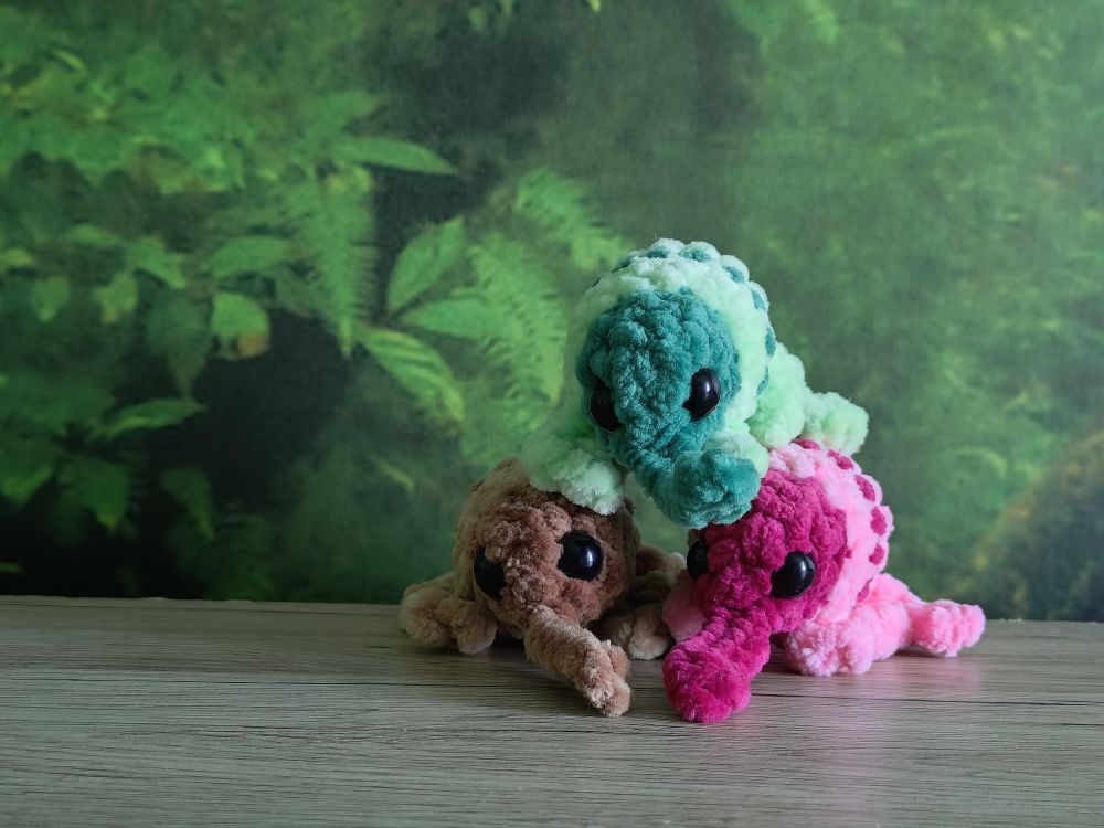 Three amigurumi weevils, one light brown, one pink, and one green