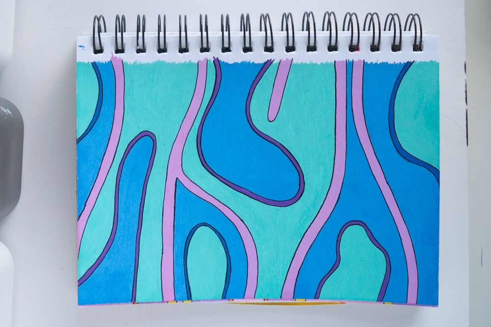 Image of a sketchbook with hand painted paper, featuring organic shapes in a few colors. Sections are split by pink organic lines. Each section typically features a blue or teal background, with a smaller alternating teal of blue blob lined in purple.