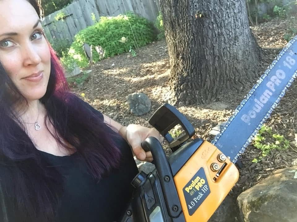 Shawna, a white woman with long dark hair, holds a chain saw. She has a devious expression with an eyebrow raised. 