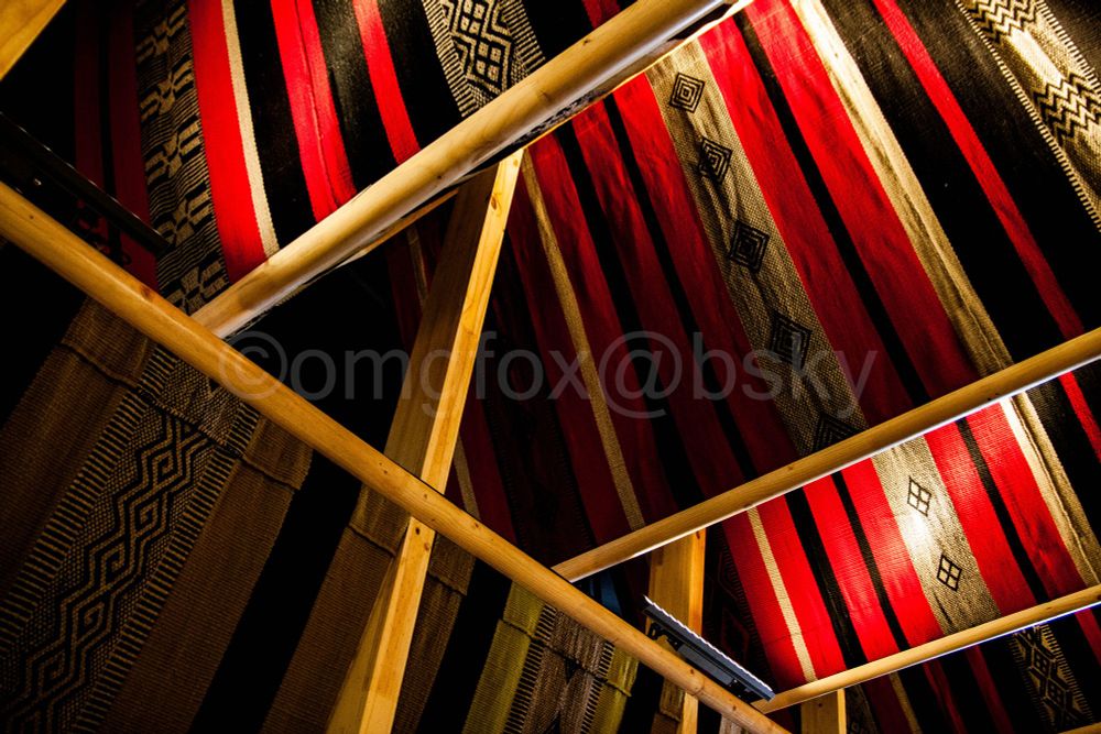 Inside view of a large, striped textile as part of Chile's pavilion at Osaka Expo. The colors are a vivid red, black, and white, with geometric patterns, strung up with a golden brown wooden frame.