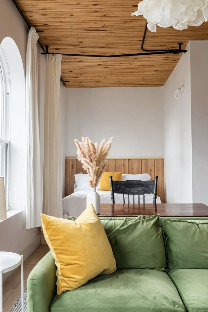 Green couch, yellow pillow, wood tones, and big curved windows are the location for this potential photoshoot