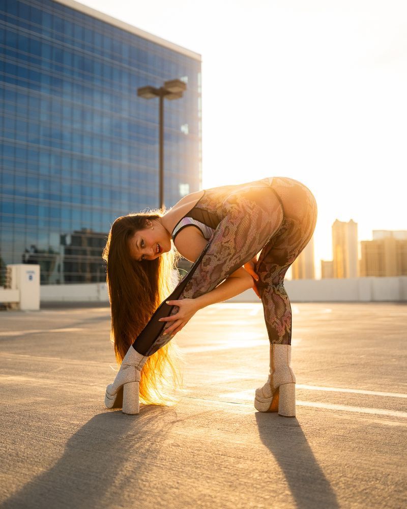 Goldie on parking garage at sunset, bending to left leg in textured bodysuit
