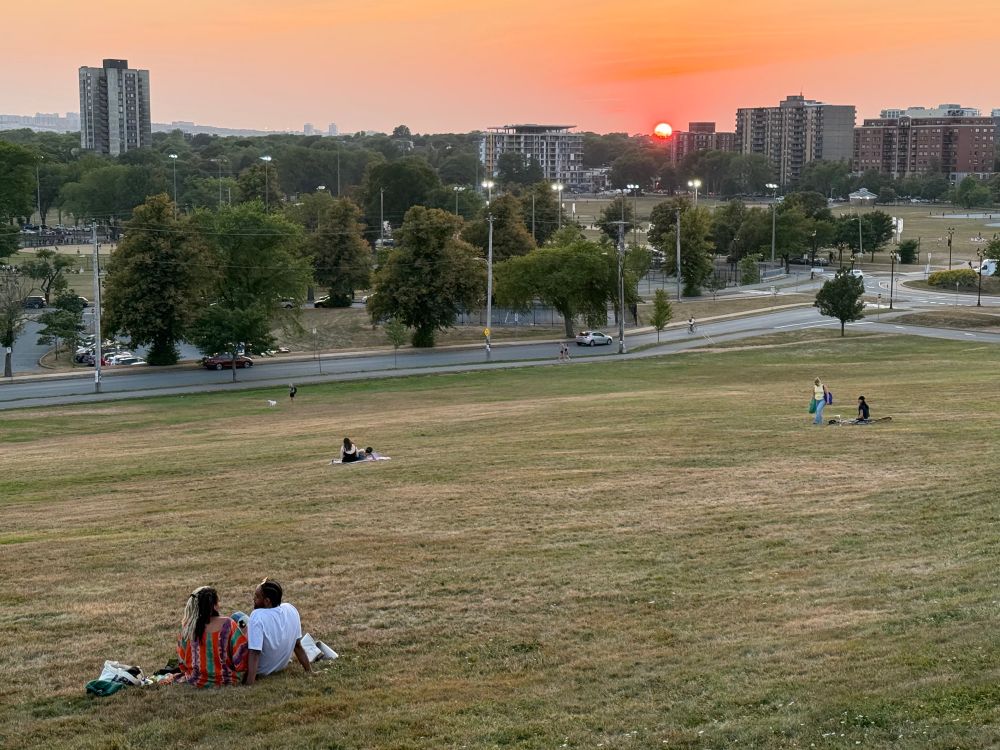 The lawn of Citadel Hill with scattered groups sitting and watching the sun dip below the horizon past the Halifax Common. 