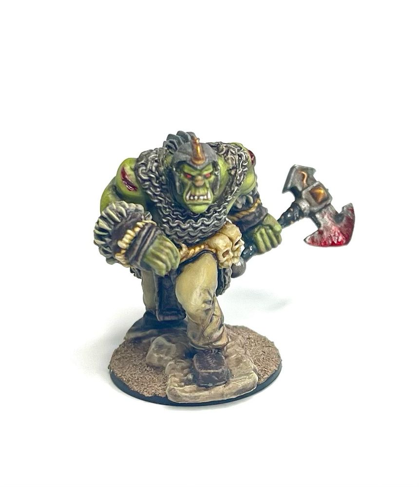 A painted green orc miniature from the front. He is marching ahead, wearing a chain shirt and wielding a bloody axe.