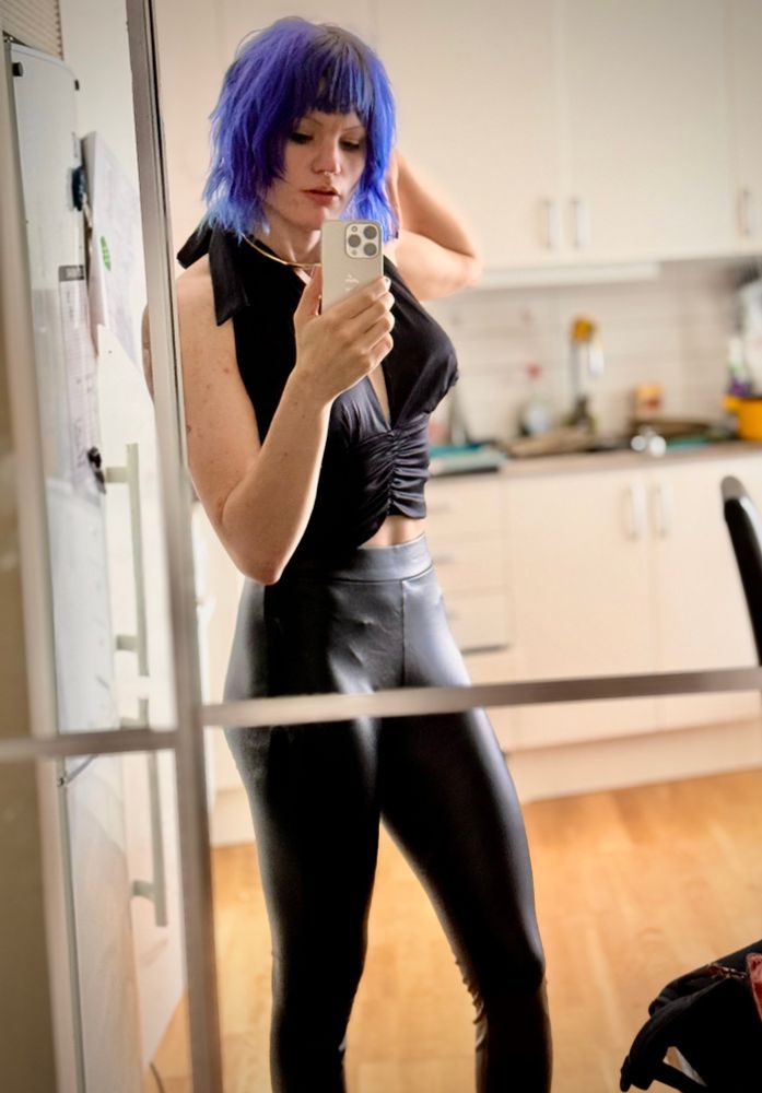 a woman with short tussled blue hair wearing black leggings and a silk haltertop she looks athletically built 