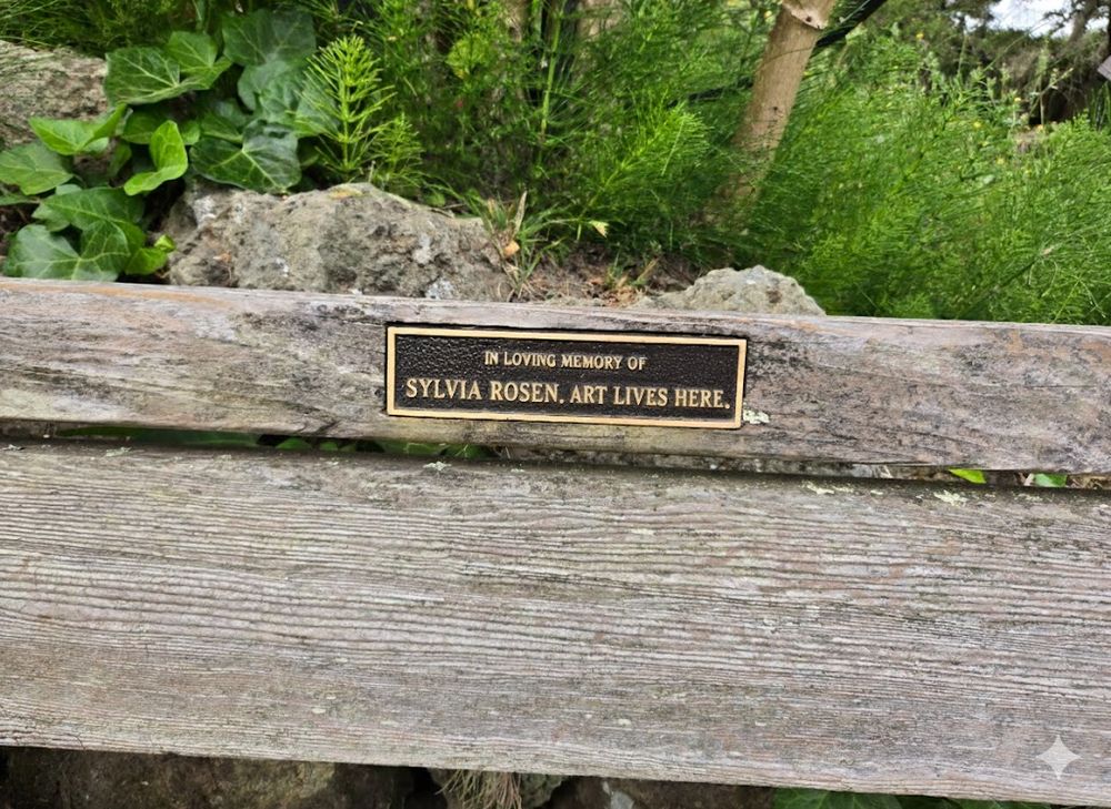 Image: A park bench with a weathered brass dedication plaque reading "In Loving Memory of Sylvia Rosen" and the epitaph, "Art Lives Here." (Photo taken by the author in the Berkeley Rose Garden; AI tool used to fictionalize names.)
