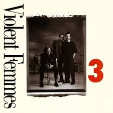 Album cover for Violent Femmes' third studio album titled '3'. A vintage black and white photograph showing three band members dressed in dark formal clothing, standing together in what appears to be a classic portrait style from an earlier era. The band name 'Violent Femmes' appears vertically in black text along the left side, while a large red number '3' is prominently displayed in the bottom right corner.
That opening, stammering guitar riff feels like the first tremor of Meddy's control beginning to slip. It's the internal whisper of Ladon, the subtle shift in the air pressure around her, the almost imperceptible tightening of the snakes in her hair. It’s not full-blown panic yet, but a deeply unsettling awareness that the normal rules are starting to bend.
As the song progresses, the tension escalates with each strum and beat. Gano's vocals, shifting between a strained near-whisper and an almost desperate yell, embody Meddy's internal struggle. It's the battle between wanting to be normal, to connect with someone like Paul without the fear of petrification, and the primal, untamed power that threatens to erupt from within her. The seemingly simple instrumentation, the acoustic guitar carrying that anxious melody, the driving bass line like a frantic heartbeat, the minimal percussion emphasizing the raw emotion, creates a sense of claustrophobia, mirroring Meddy's feeling of being trapped within her own changing body.

That explosive, almost violent strumming of the guitar during the instrumental break is the closest sonic equivalent to Meddy's full Gorgon transformation. It's the moment when the snakes fully awaken, when her eyes begin to glow, and the world around her is in danger of turning to stone. The song offers no release; it just ends abruptly, leaving that raw, unresolved tension hanging in the air, much like the aftermath of one of Meddy's uncontrolled outbursts.