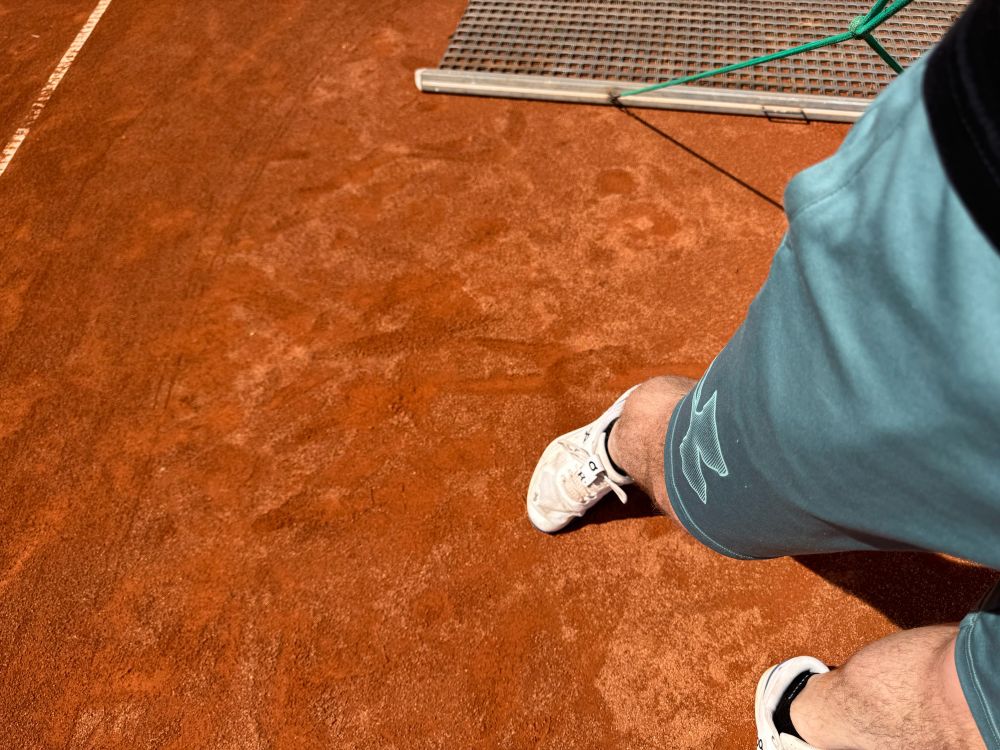 Es ist ein Sand-Tennisplatz zu sehen, der gerade abgezogen wird