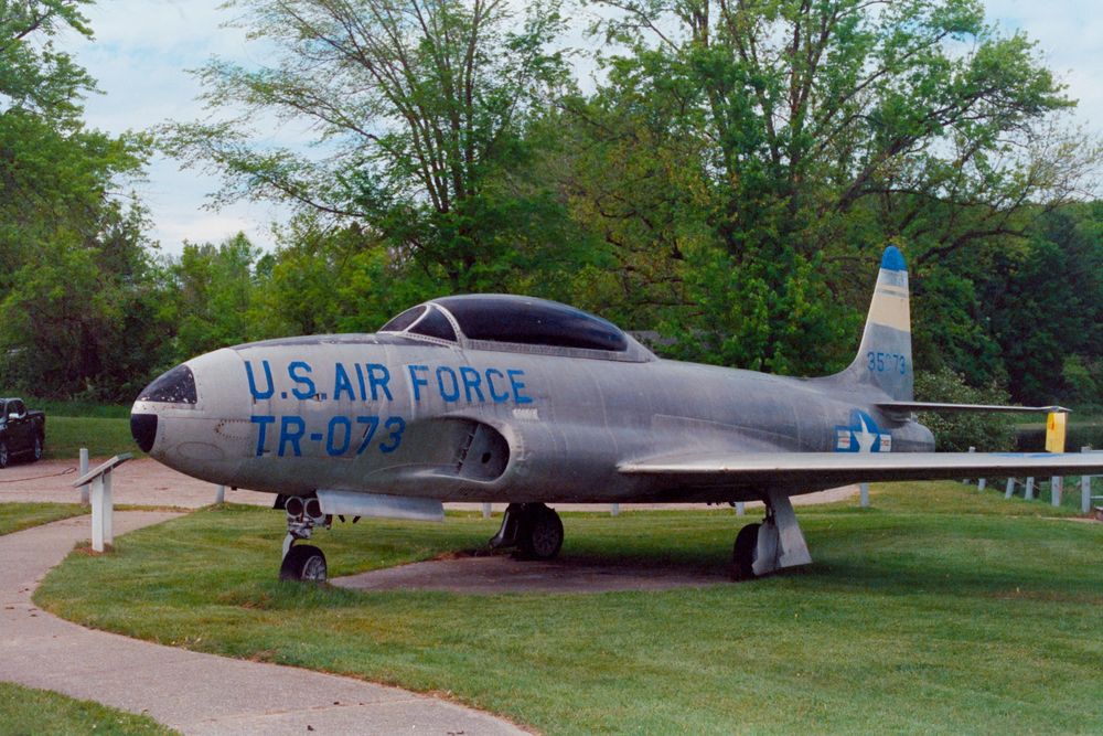 A color film photo of a retired Lockheed P-80 Shooting Star, on permanent display in a small lakeside park in Hart, Michigan, USA