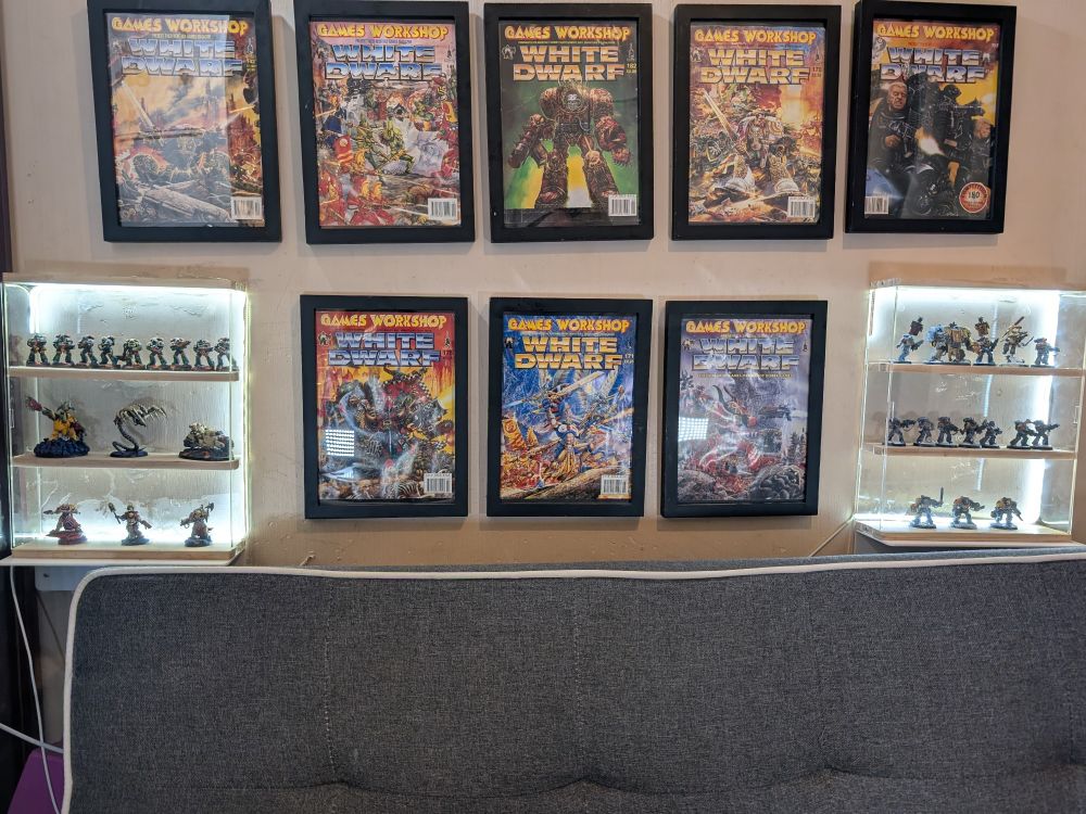 A wall display of two display cabinets and eight framed white dwarf covers from the 90s