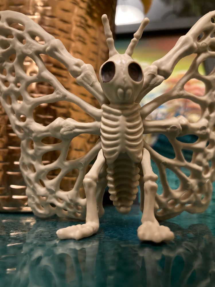 A Halloween decoration of a butterfly entirely made of bone shapes. It has a ribcage and pincers, and is standing up on two little legs with knees and flat webbed feet.
