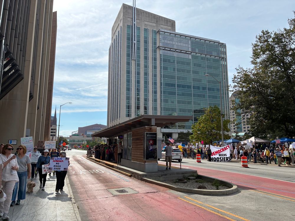 A crowd near a bus rapid transit station. One sign says “Democracy needs Hoosiers.”