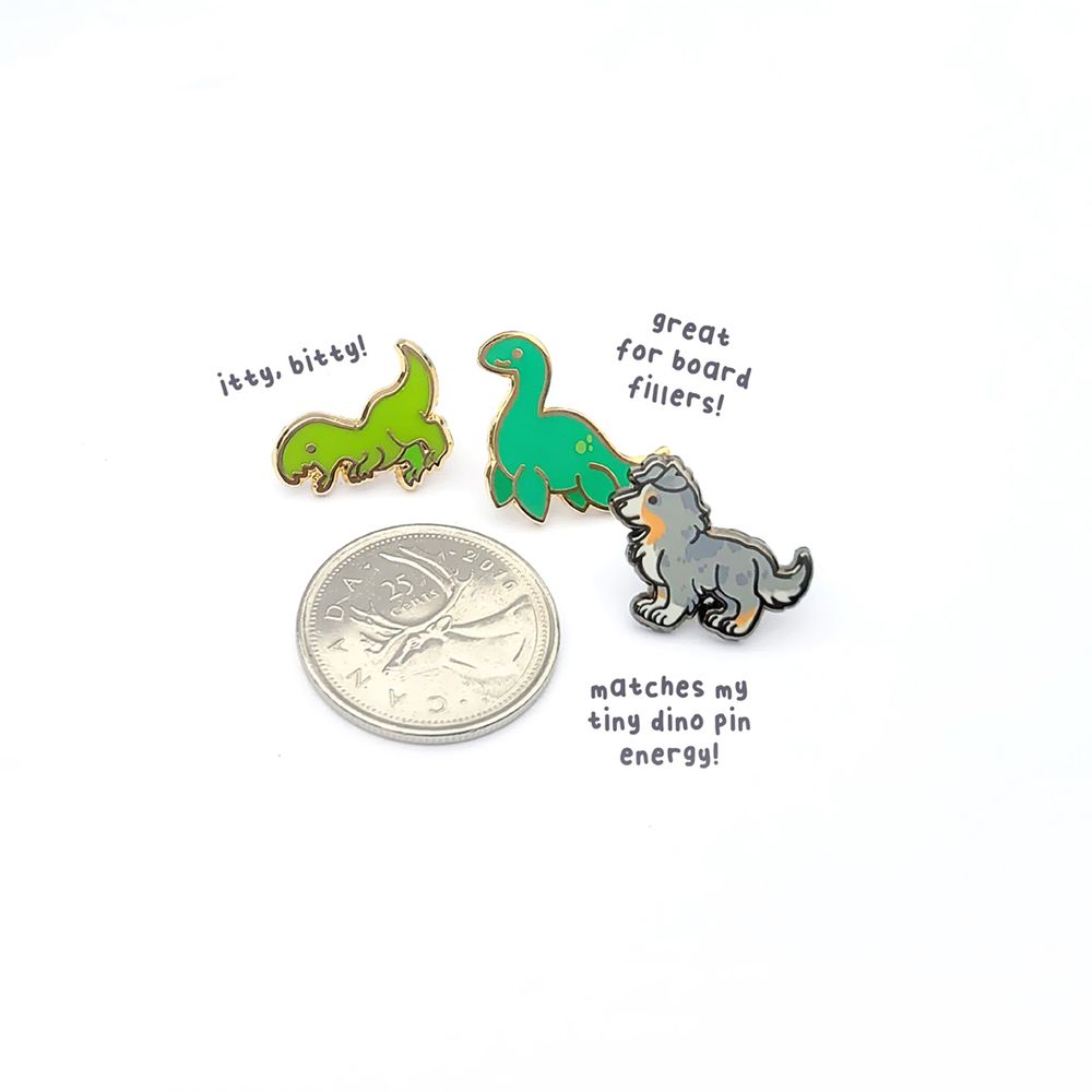 Little tiny dinosaur and doggo enamel pins beside a quarter for size comparison.