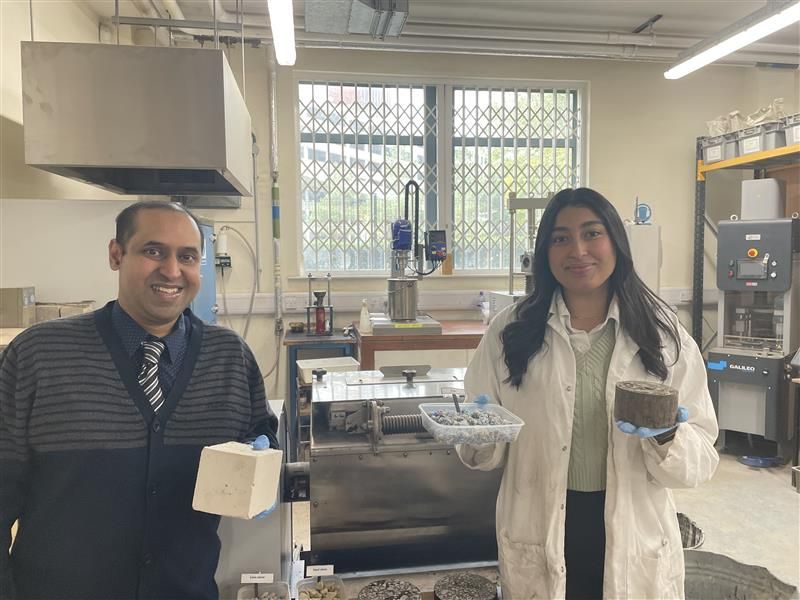 Dr Ash Ahmed and Habiba El-Gharably holding waste medical material (floc) which they are repurposing as a low carbon aggregate in civil engineering materials - in Habiba's right hand she is holding floc, in her left hand she is holding asphalt concrete for roads and highways, and Ash is holding concrete, which both contain waste floc.