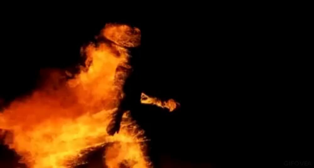 a person is standing in front of a large flame in the dark .