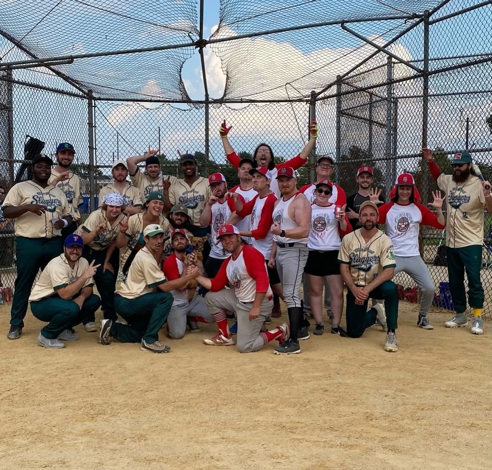 Group photo of two Philadelphia Sandlot Baseball teams (Kensington Kayfabe in red and white, Wissahickon sluggers in green and off-white) in front of a backstop