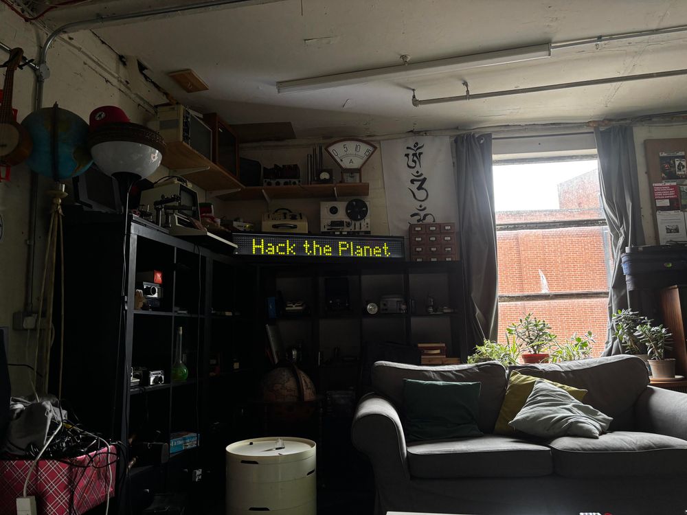 The flip dot display looking fabulous in the comfy area, displaying the message "hack the planet"