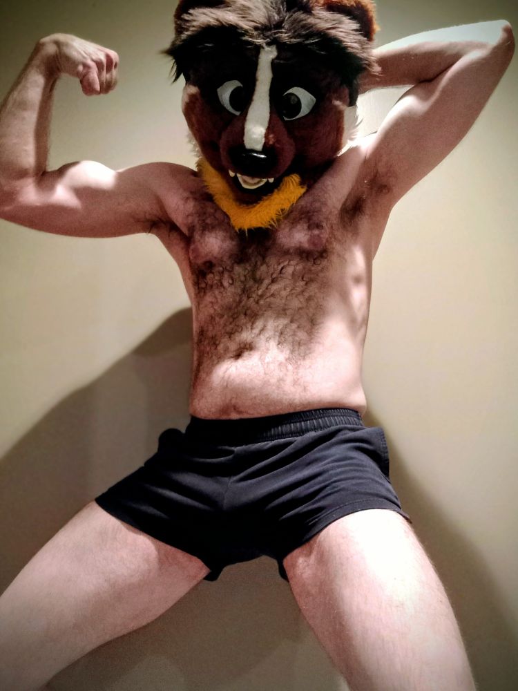 Shirtless man with weasel fursuit head, flexing his right arm and putting his left hand behind his head, with his legs in view.