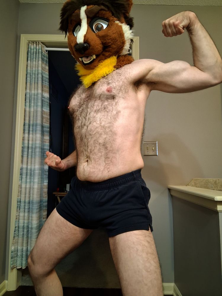 Shirtless man with weasel fursuit head, flexing one arm while puffing out his chest and turning partly to the side.
