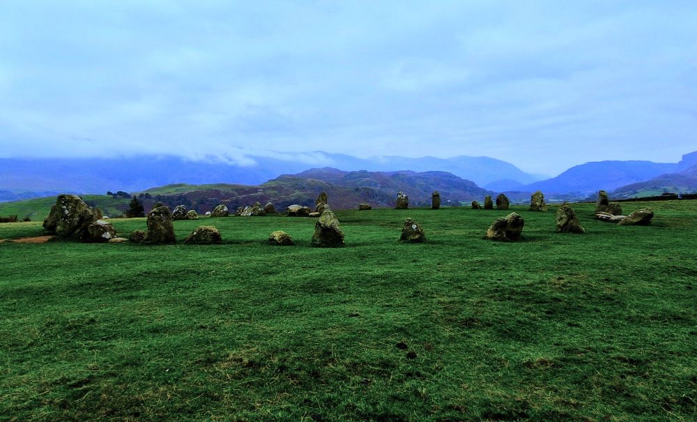A circle of oddly shaped, rough stones on a grassy hill. It feels open and quiet, with soft winds and a cold and mysterious atmosphere. Around it, hills are shrouded in an autumnal haze of mist and clouds. 
