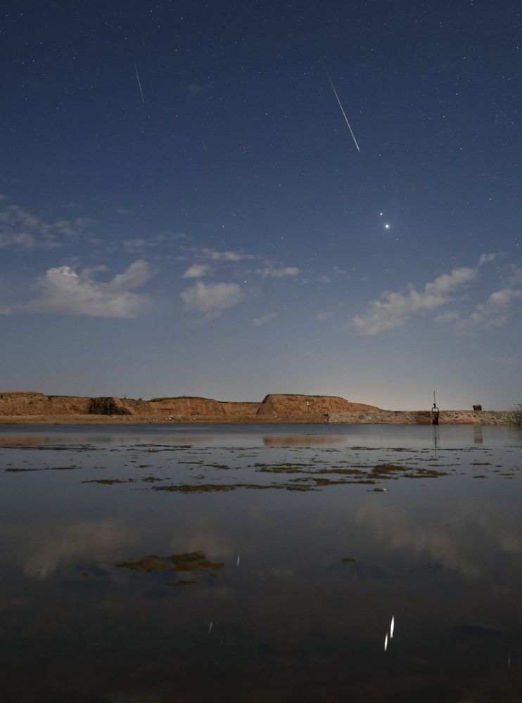In the predawn sky on August 13, two planets were close. And despite the glare of a waning gibbous Moon, bright Jupiter and even brighter Venus were hard to miss. Their brilliant close conjunction is posing above the eastern horizon in this early morning skyscape. The scene was captured in a single exposure from a site near Gansu, China, with light from both planets reflected in the still waters of a local pond. Also seen against the moonlight were flashes from the annual Perseid Meteor Shower, known for its bright, fast meteors. Near the much anticipated peak of activity, the shower meteors briefly combined with the two planets for a celestial spectacle even in moonlit skies.