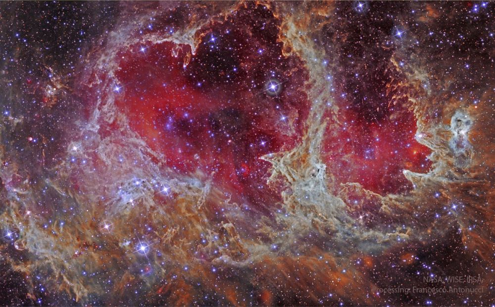 A star field is shown in infrared light. In the center is an extremely complex nebula that is outlines an iconic heart. Glowing gas shades the center of the heart red. Please see the explanation for more detailed information.