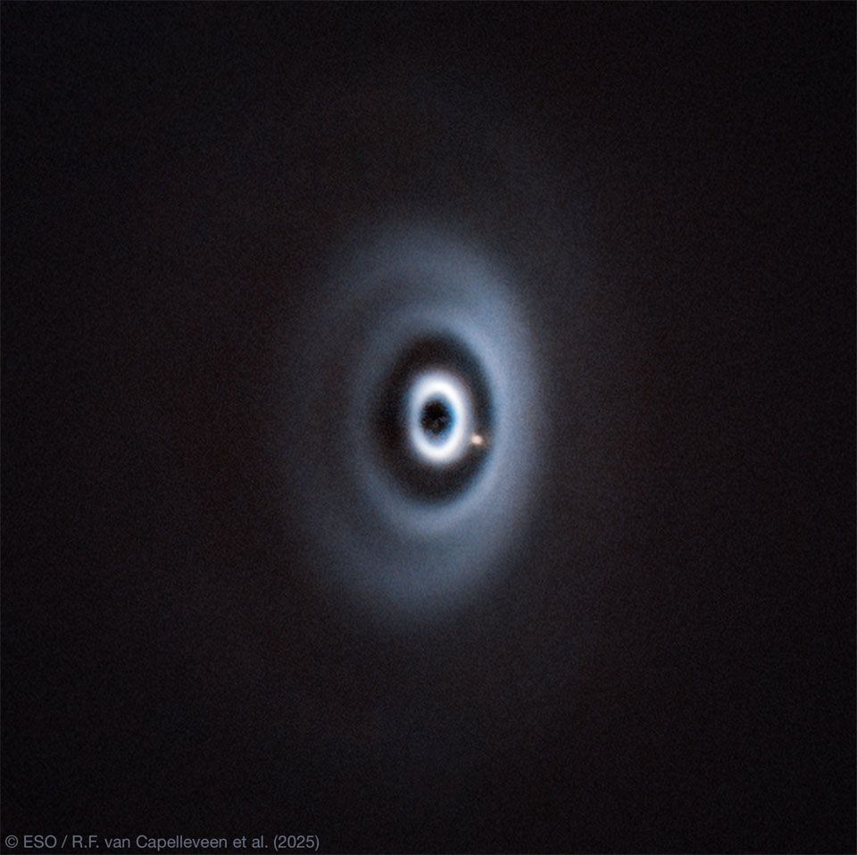 A dark field has a series of light-colored elliptical rings in the center. Between two of the rings is a yellow-colored spot. Please see the explanation for more detailed information.