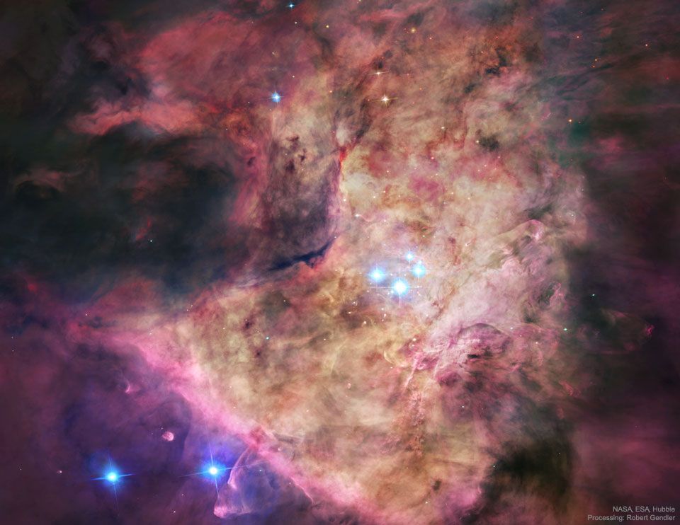 A bright nebula occupies the center of the frame. The nebula is complex but roughly tan in the center and red around the edges. In the center are four bright blue stars. Please see the explanation for more detailed information.