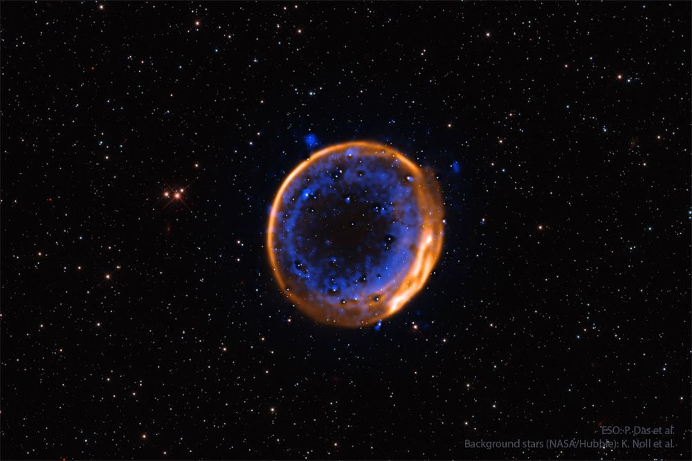 A nearly circular nebula with two rings is shown. The outer ring appears orange while while the inner rings is more complex and appears blue. Please see the explanation for more detailed information.