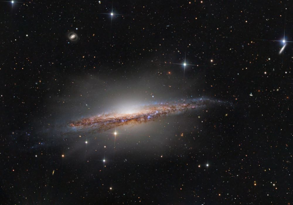 Big, beautiful spiral galaxy NGC 1055 is a dominant member of a small galaxy group a mere 60 million light-years away toward the aquatically intimidating constellation Cetus. Seen edge-on, the island universe spans over 100,000 light-years, a little larger than our own Milky Way galaxy. The colorful, spiky stars decorating this cosmic portrait of NGC 1055 are in the foreground, well within the Milky Way. But telltale pinkish star forming regions and young blue star clusters are scattered through winding dust lanes along the distant galaxy's thin disk. With a smattering of even more distant background galaxies, the deep image also reveals a boxy halo that extends far above and below the central bulge and disk of NGC 1055. The halo itself is laced with faint, narrow structures, and could represent the mixed and spread out debris from a satellite galaxy disrupted by the larger spiral some 10 billion years ago.