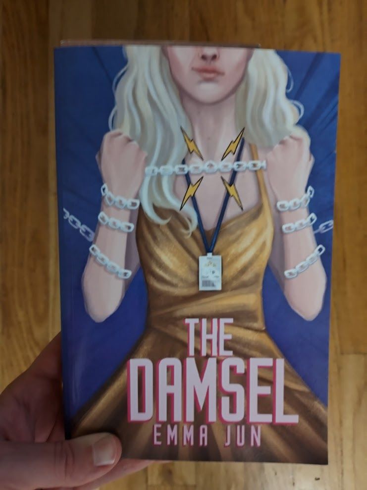 The cover of Emma Jun's The Damsel. A blonde woman in a golden dress holds a chain like a garrote.