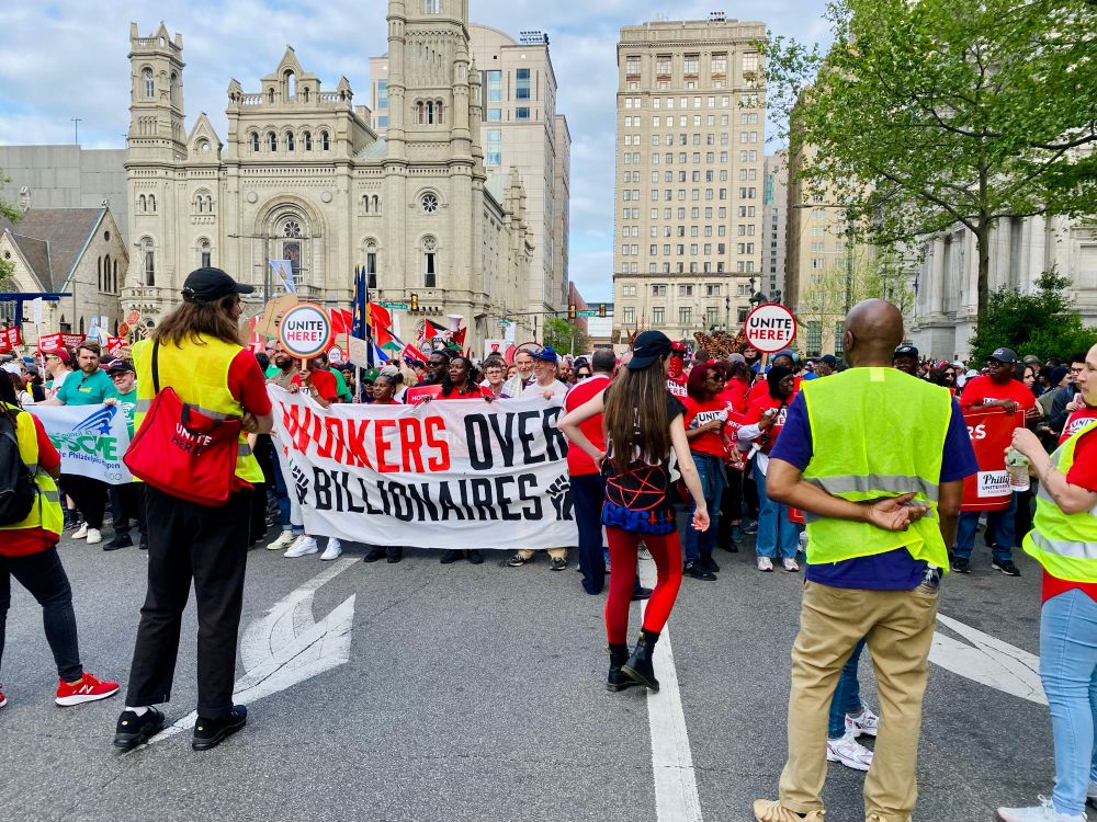 Front view of the Philly May Day 2025 March with many union members holding a banner that reads Workers Over Billionaires (and city hall in the background)