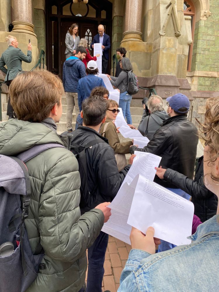A line of Penn employees and students holding up a 30-foot-long printed petition signed by well over 1,000 workers, marching up the steps to College Hall