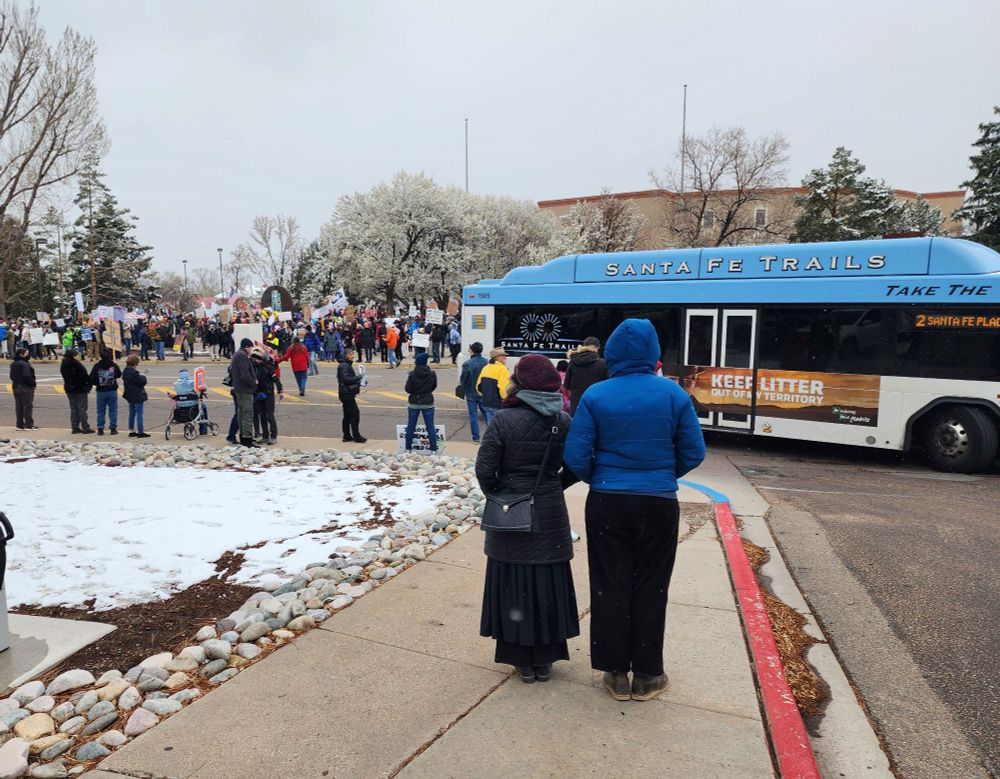 Large crowd of protesters at the New Mexico State Capitol grounds. Santa Fe Trails city bus in shot.