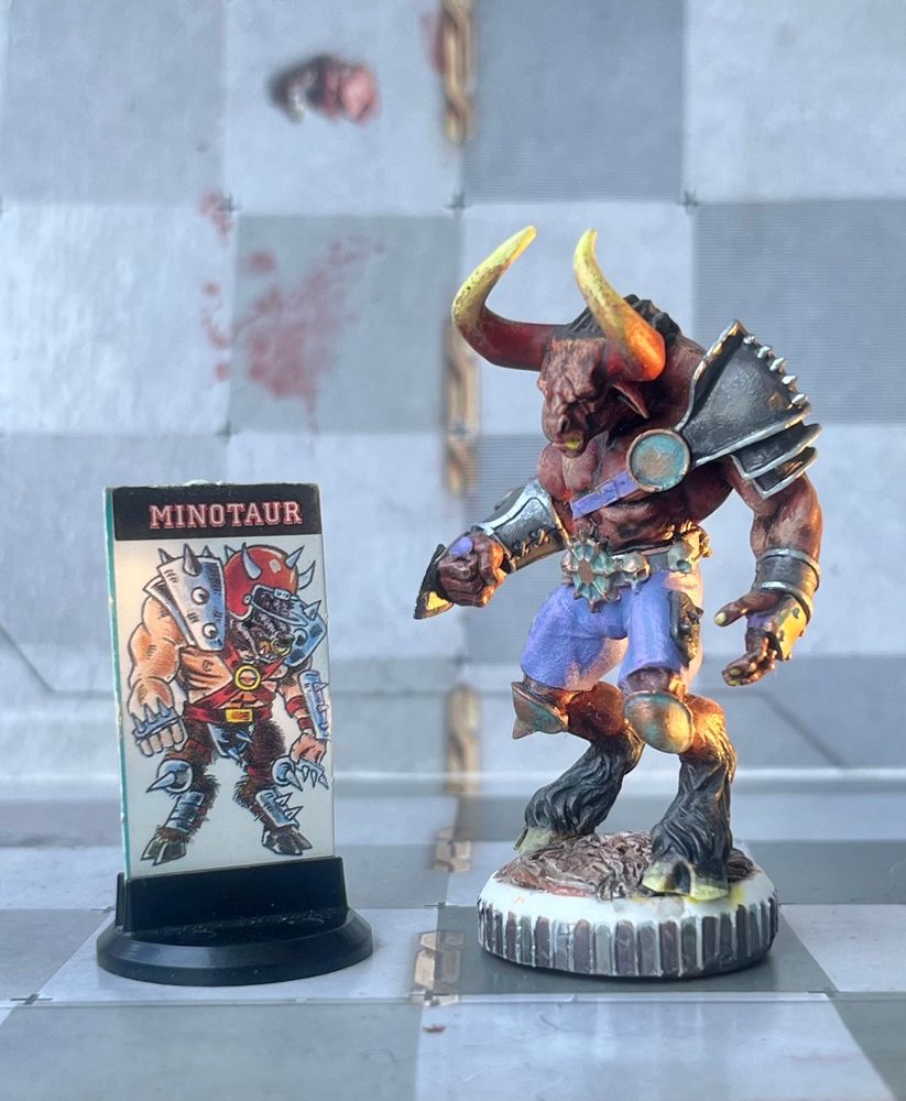 Two ways to represent Minotaur in the board game of Blood Bowl. On the left is cardboard stand with printed image of Minotaur on plastic base, distributed with Death Zone expansion in 1987. On the right metal miniature by Willy Miniatures from 2013.