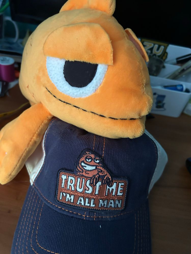 Klaus plush with a hat with Klaus on it that says “Trust me, Im all man”