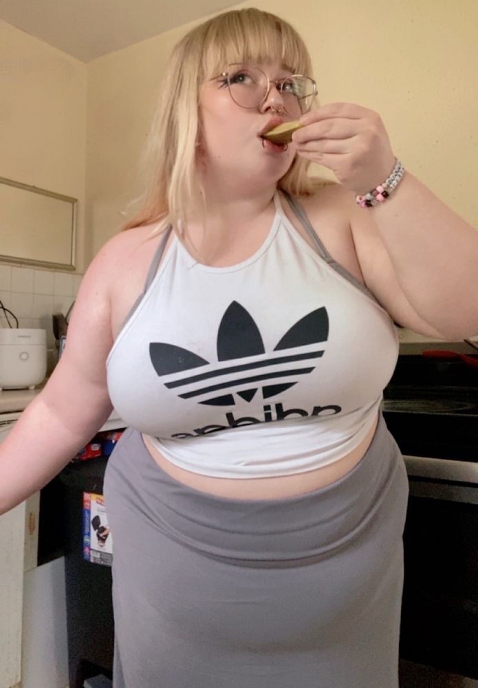 Chincherri (blonde plus size woman) eating a pickle in her kitchen