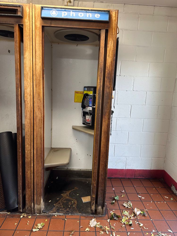 A pay phone seen in the wild. It's a phone attached to the wall, in a small closet-like area. You can close the door to make calls in relative privacy