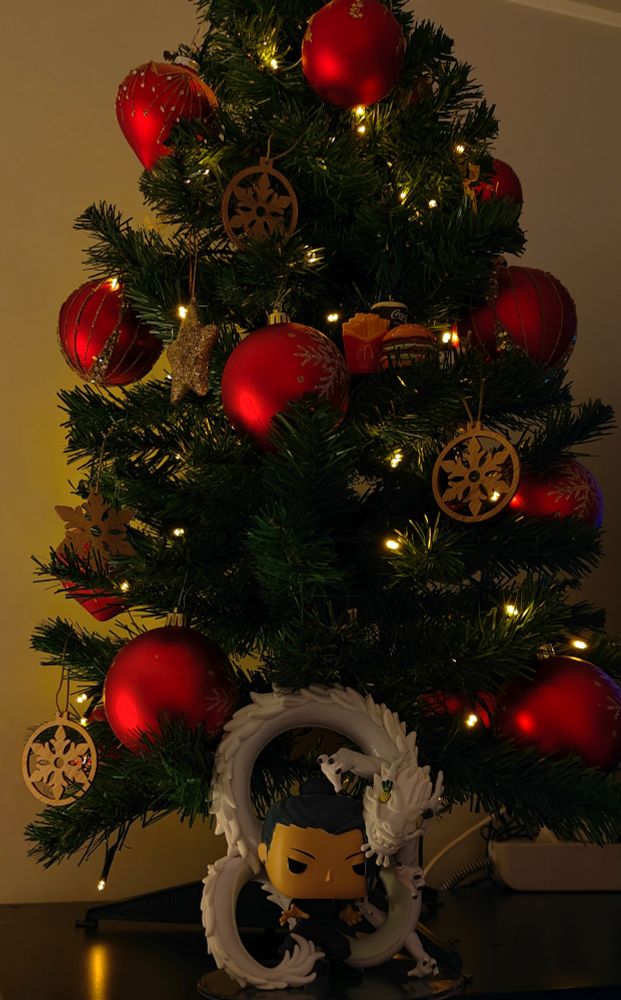 Little christmas tree with red christmas balls, wooden snowflake ornaments and lights. With a Geto Funko doll with his dragon from the series, Jujutsu Kaisen